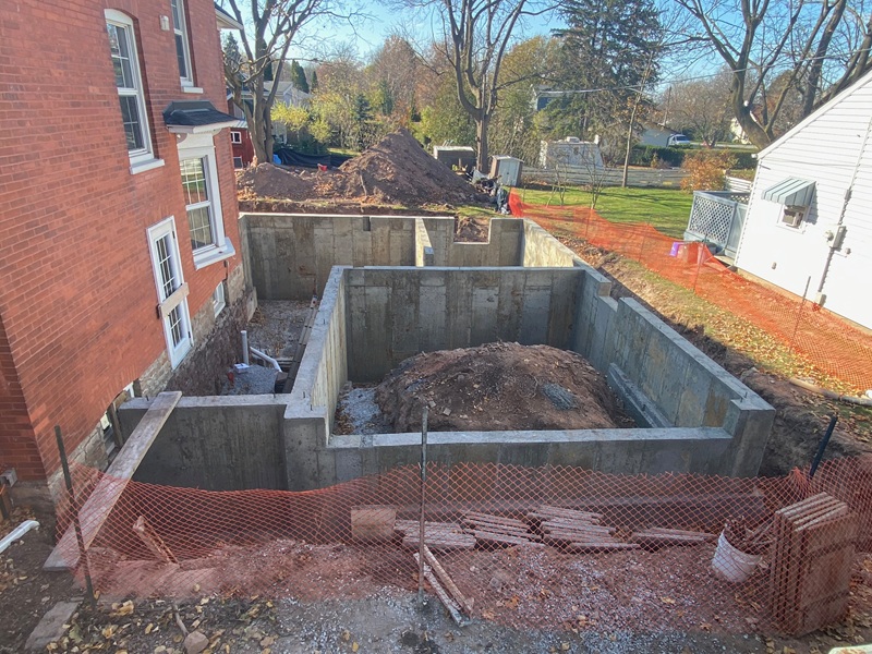 New residential concrete foundation walls beside an existing brick home